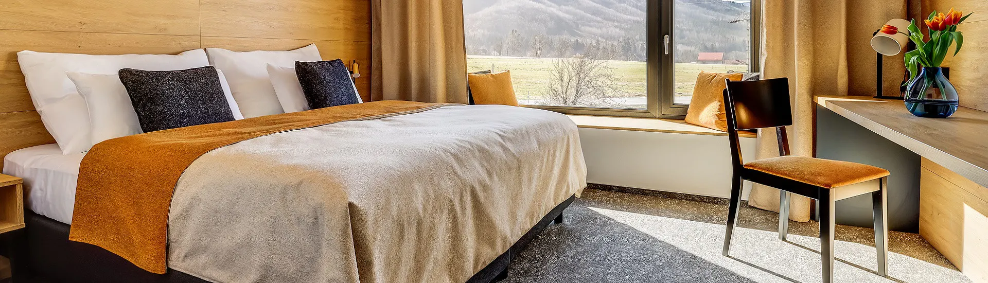Hotelový pokoj s dřevěným obkladem a velkým oknem s výhledem na beskydské louky