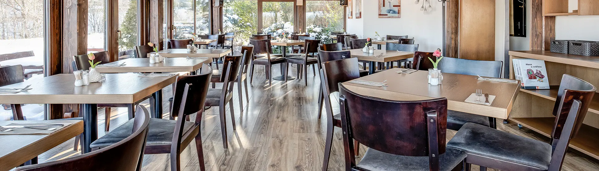 Interiér restaurace Maralák s dřevěnými stoly a prosklenou stěnou do zasněžené zahrady