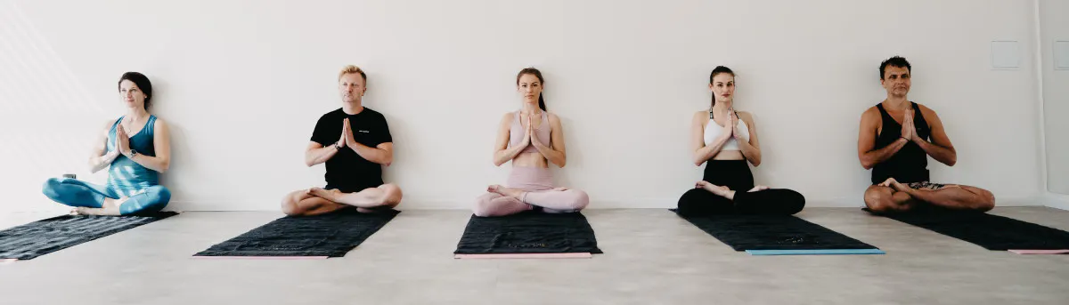 Skupina cvičenců v meditaci vsedě ve světlém jógovém sále